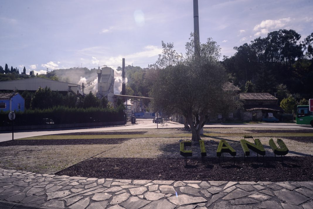 Las letras de Ciañu en una zona ajardinada, con la coquería de Química del Nalón al fondo.