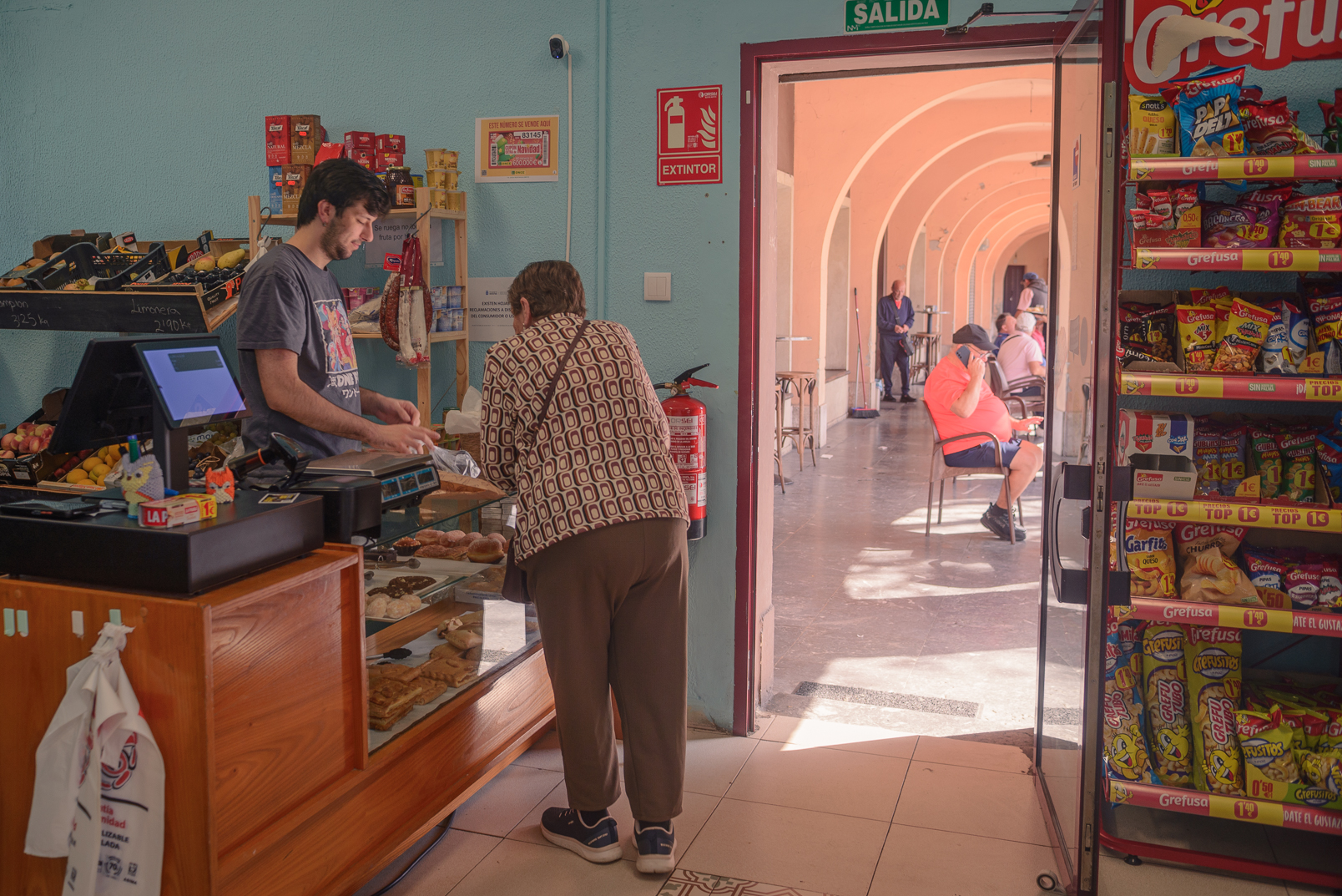Una clienta compra en una tienda de alimentación con vistas a los soportales de la Plaza Mayor de Llaranes.